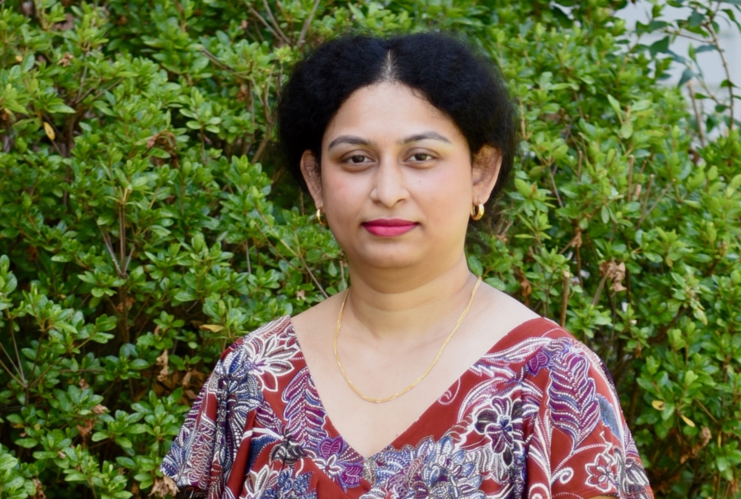 a woman in a patterned dress posing for a portrait in front of a bush.