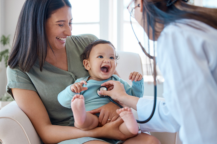 A baby being held by their mother as a pediatrician listens to their heartbeat with a stethoscope.