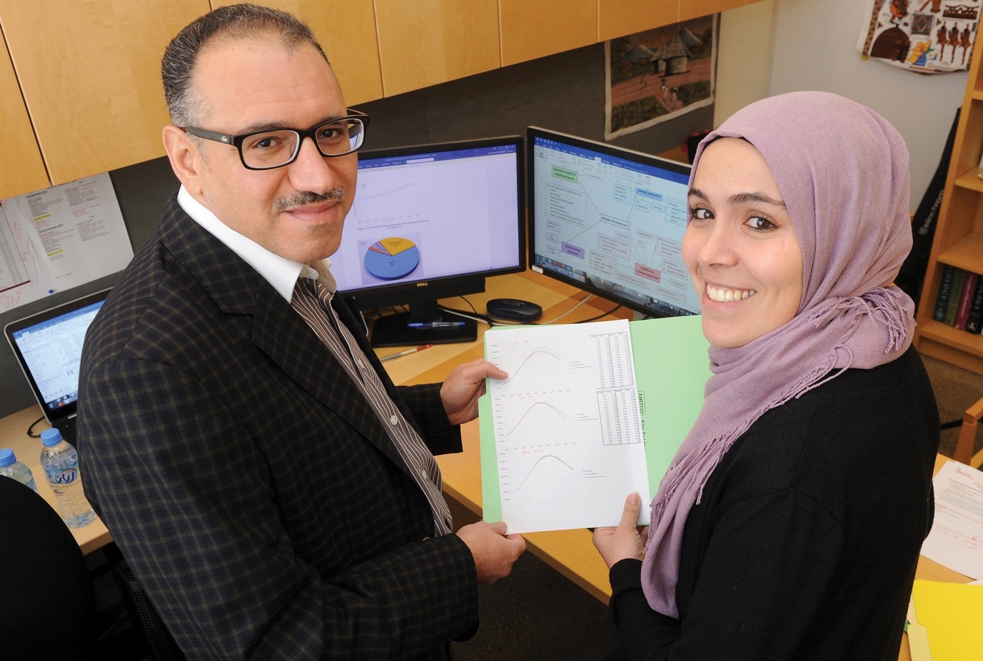 Laith Abu-Raddad and Susanne Awad holding a paper with charts and graphs