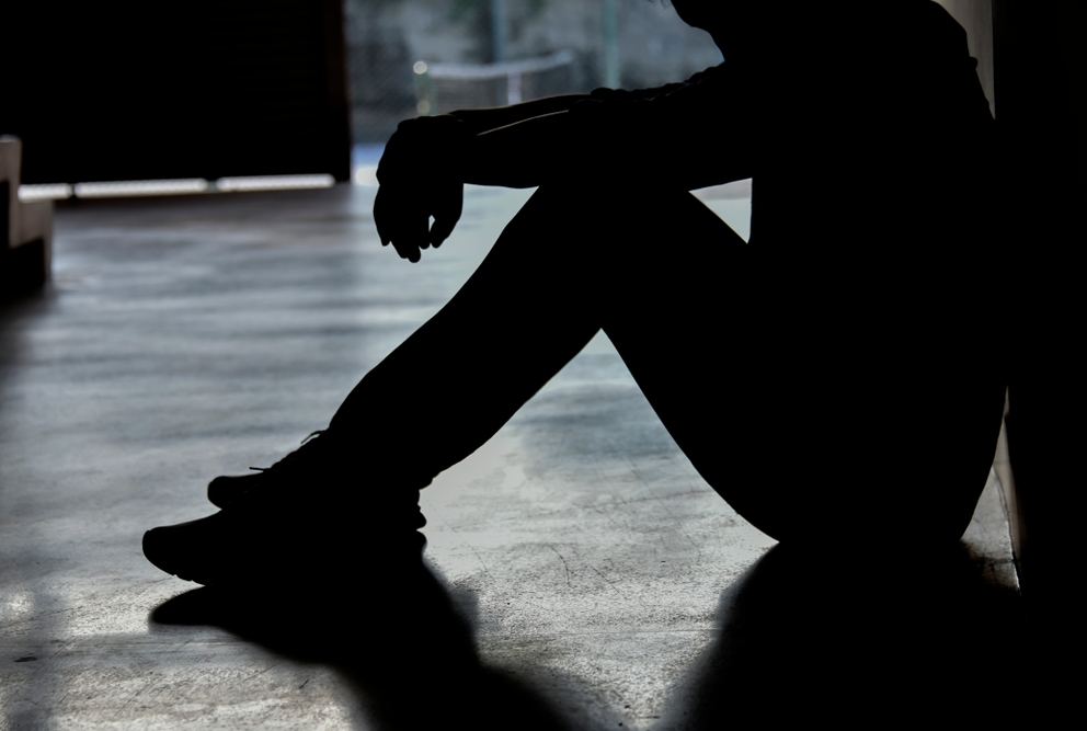 silhouette of a person sitting on the floor with their knees bent towards their chest