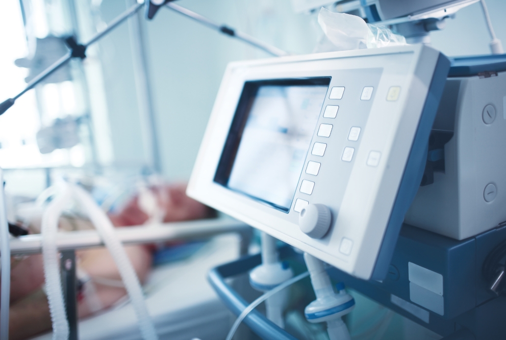 closeup of monitor beside patient bed with patient on a respirator