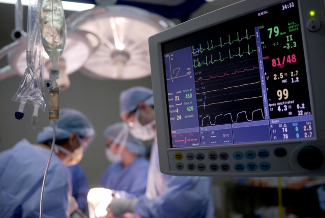 close up of vital signs monitor while surgery is performed in the background