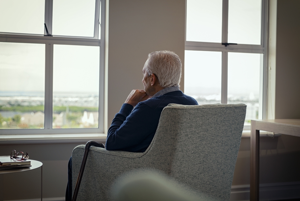 an elder man looking out a window deep in thought