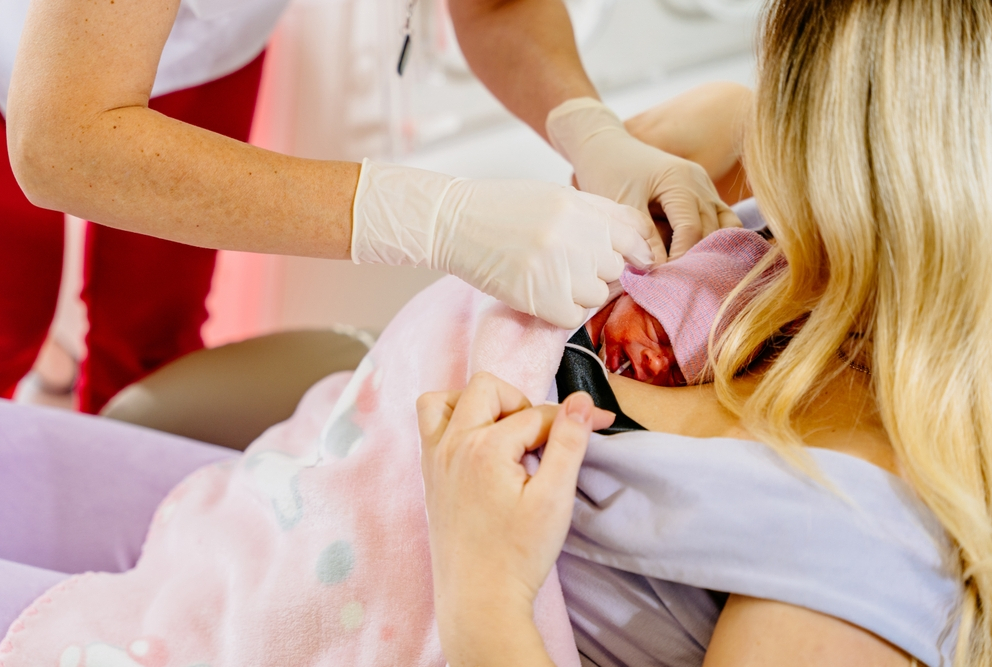gloved hands attending to baby laying on woman's chest