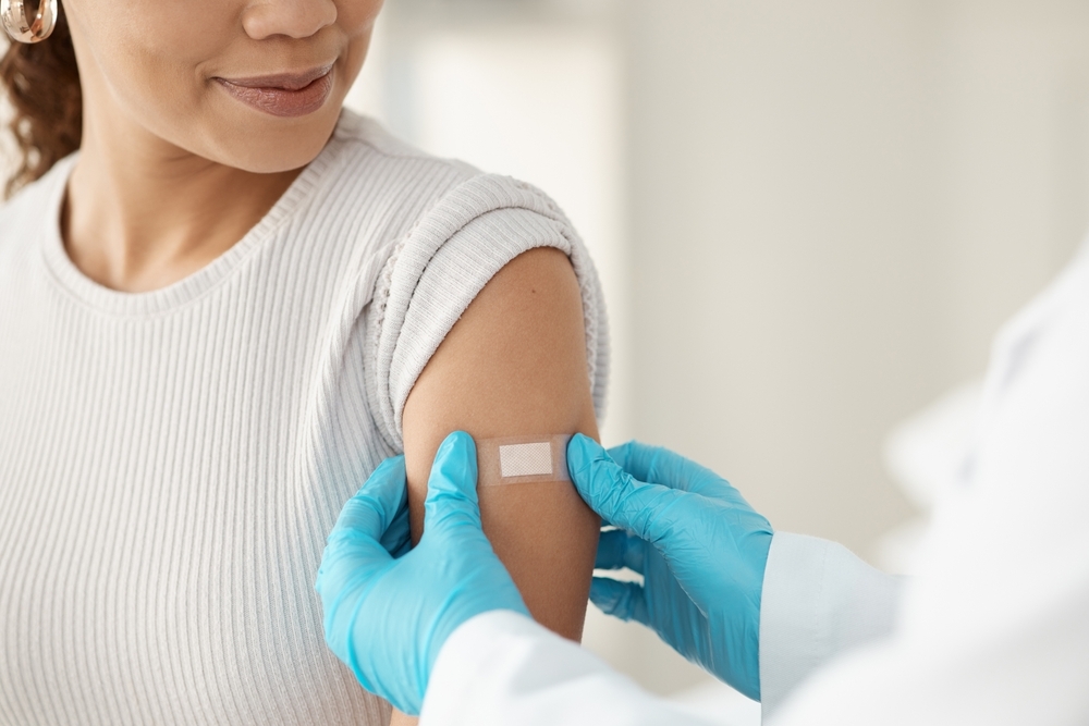 person with gloves placing an band-aid on a woman&#039;s upper arm