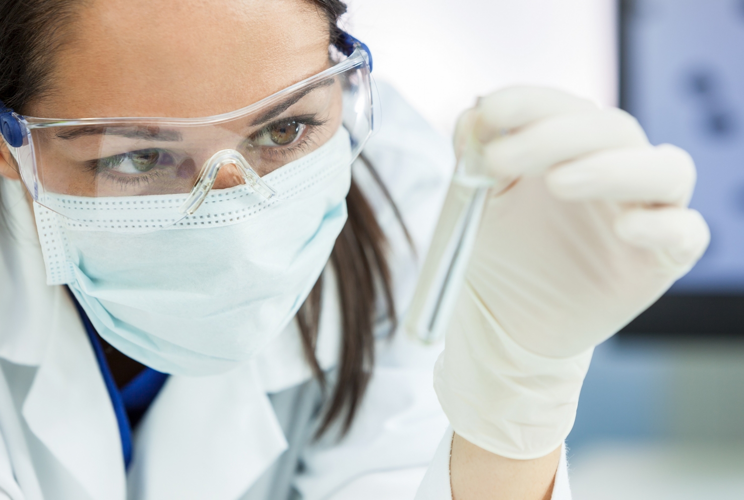 a woman wearing a protective face mask holding a test tube in a lab