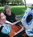 Nancy and Maggie Worthen sitting in a park. Maggie has a blue circle painting in front of her