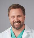 headshot of a physician wearing a white coat and green scrubs