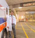 a man smiling for a photo in front of an emergency room