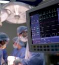close up of vital signs monitor while surgery is performed in the background