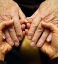 Younger hands gently holding elderly hands